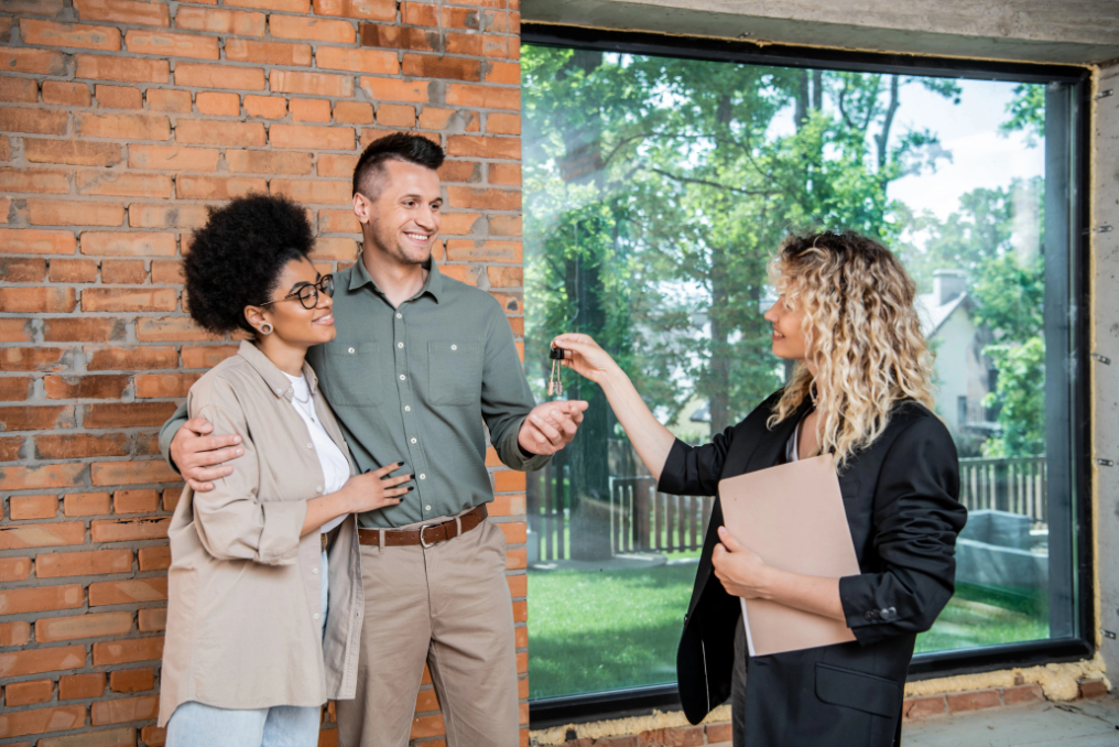 Real estate broker with documents giving keys from new house to pleased multicultural couple